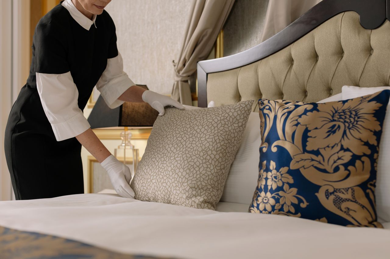 gallery-01 A chambermaid arranges pillows in a luxurious hotel room, showcasing comfort and elegance.