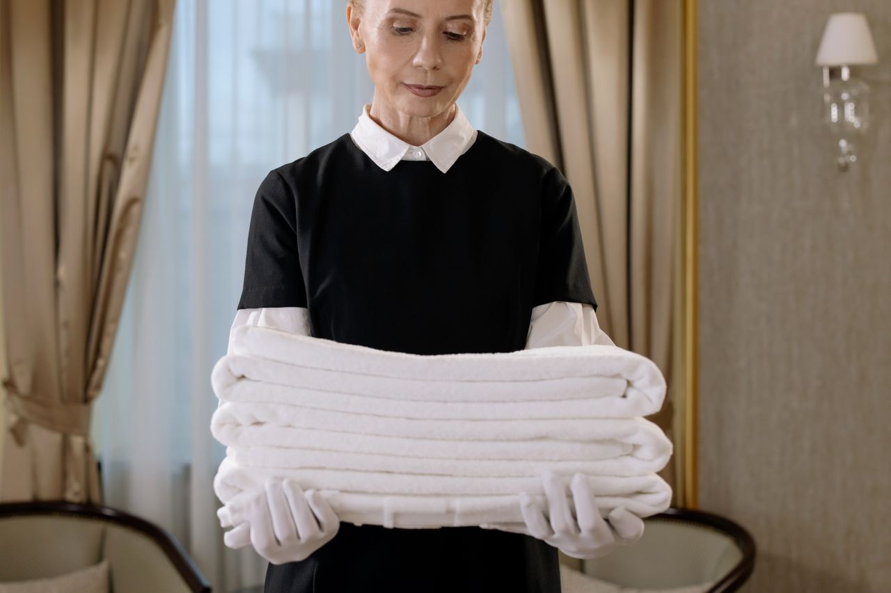 gallery-04 Professional housekeeper holding a stack of fresh towels in a luxurious hotel room, showcasing elegance and service.