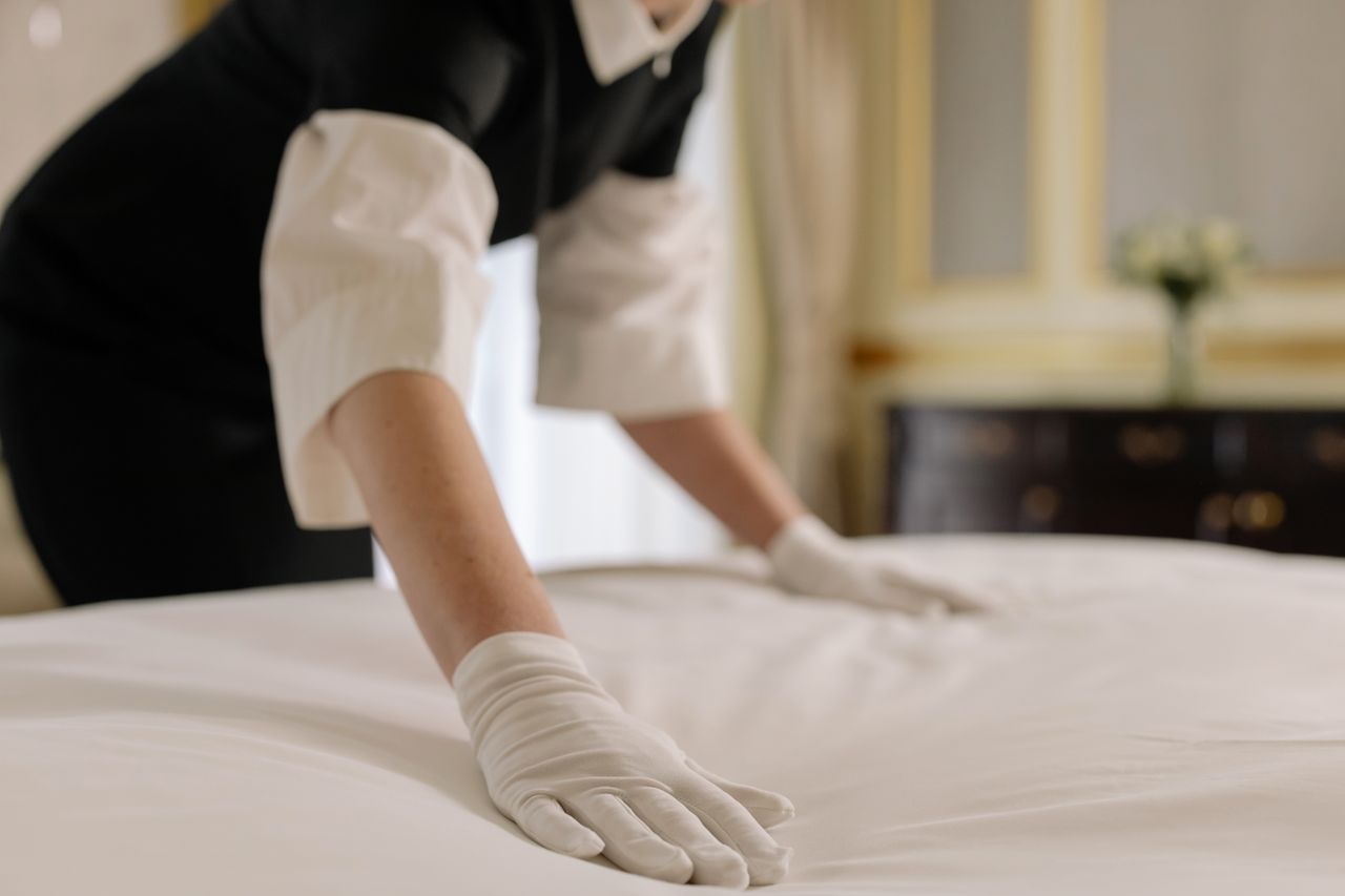 home-img A housekeeper straightening the bed linens in a well-appointed hotel room.